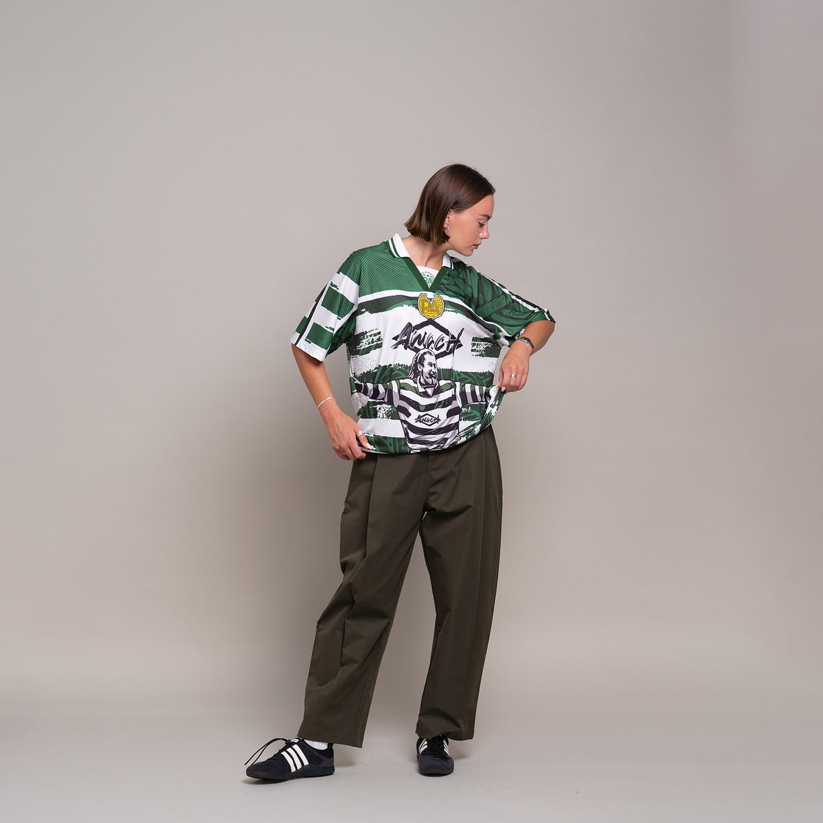AMACH Rebel Athletics Larsson jersey, green and white hooped 90s-style football shirt, front, styled with wide-leg trousers