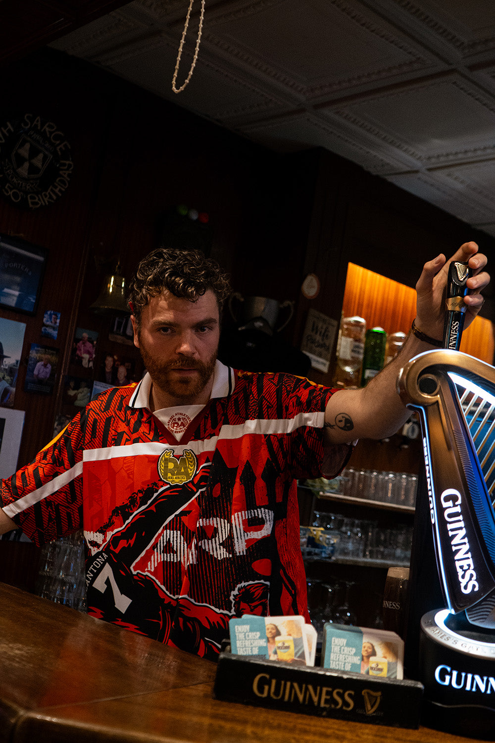AMACH Rebel Athletics Cantona jersey, red and black 90s-style football shirt, worn at the bar beside a Guinness tap