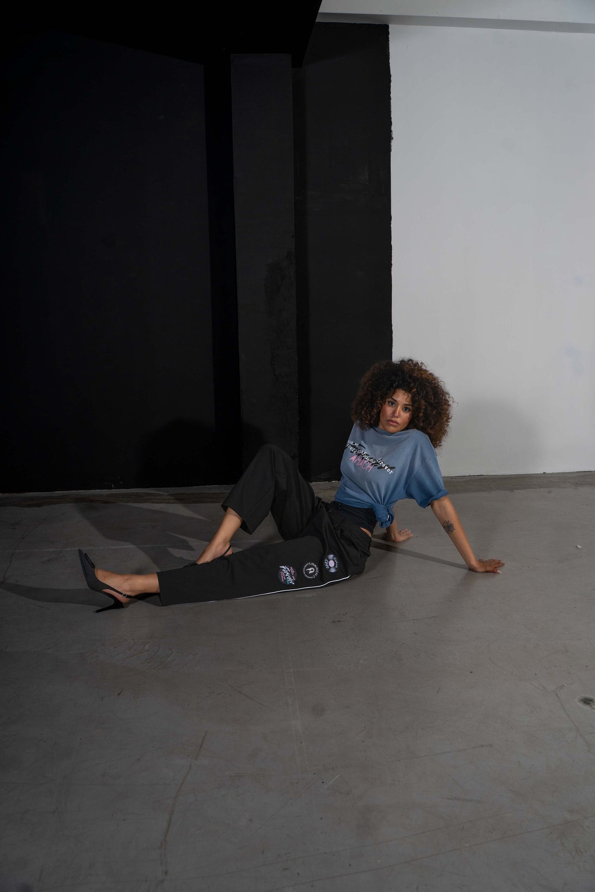 Model sitting on the studio floor in AMACH Euphoric Love slacks, showing the patches